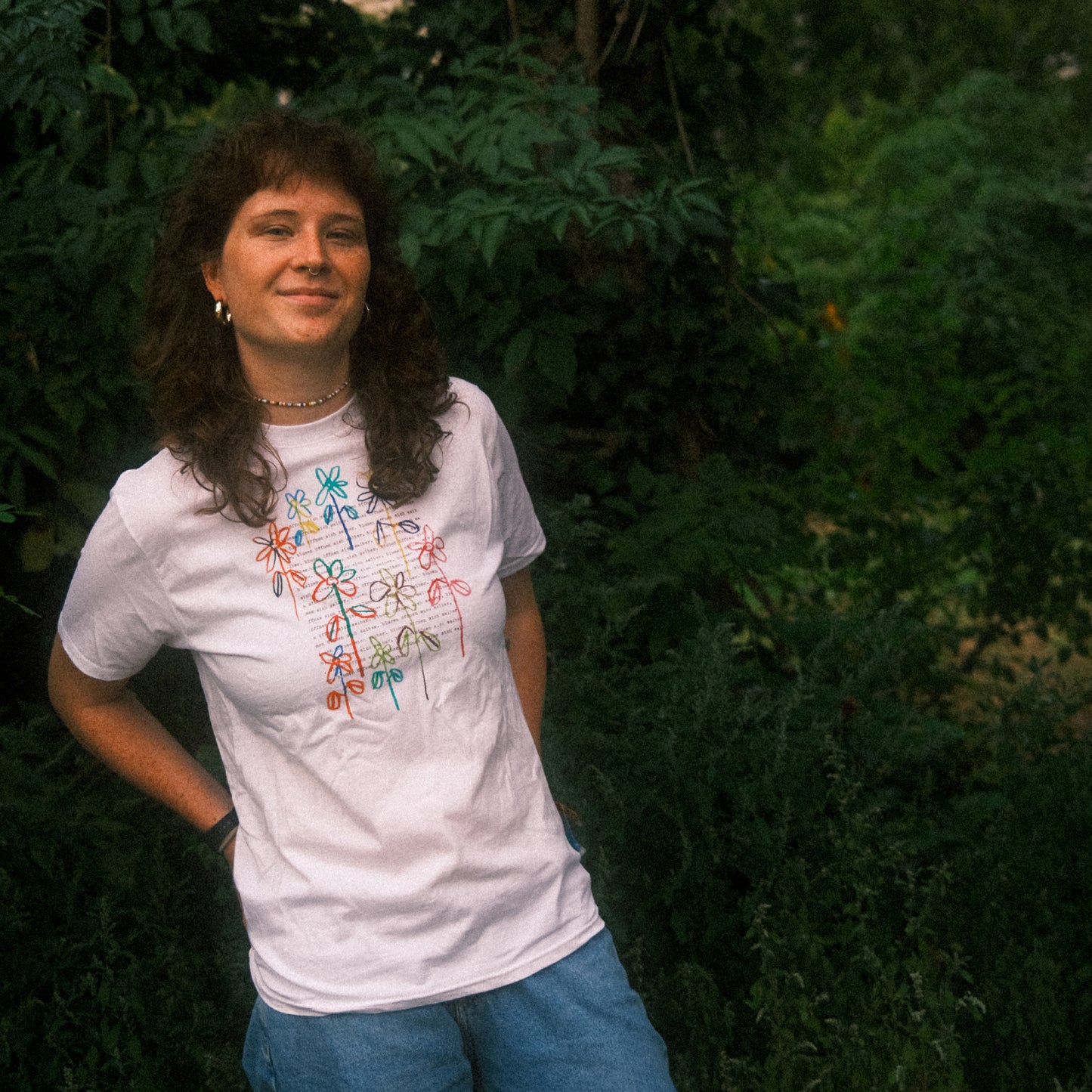 Ganzkörper im Grünen: weißes T-Shirt mit großem Blumenprint, entspannter Regular-Fit zu Jeans.