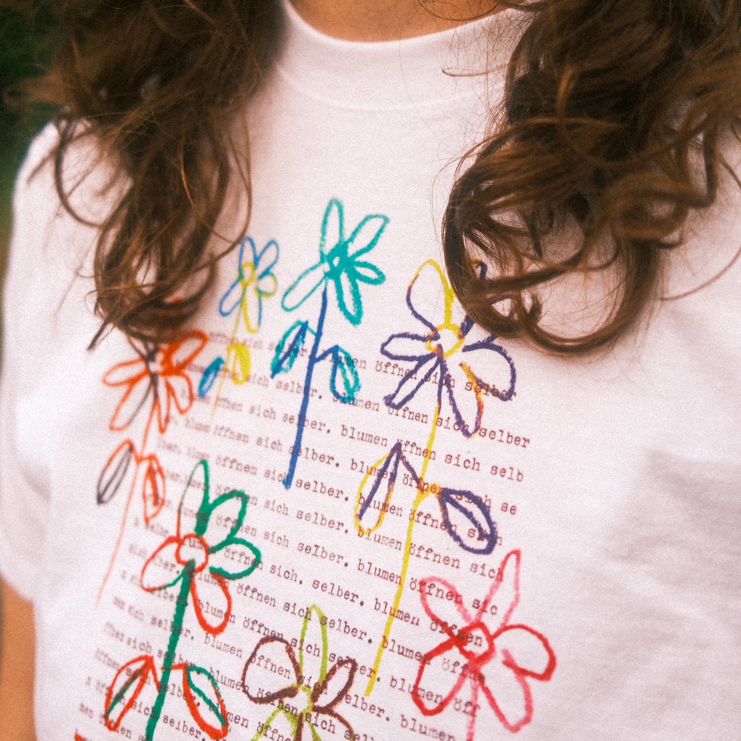 Detail Brustbereich: bunter Blumen-Blockprint auf weißem T-Shirt, Linienzeichnung über Text.