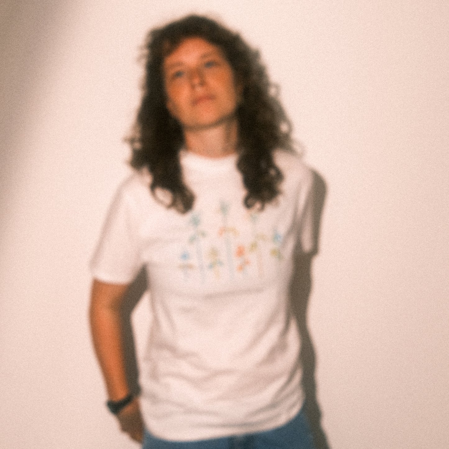 Unscharfes Ganzkörperbild: weißes T-Shirt mit farbigem Blumenprint; Motiv erkennbar, weicher Blur-Effekt.