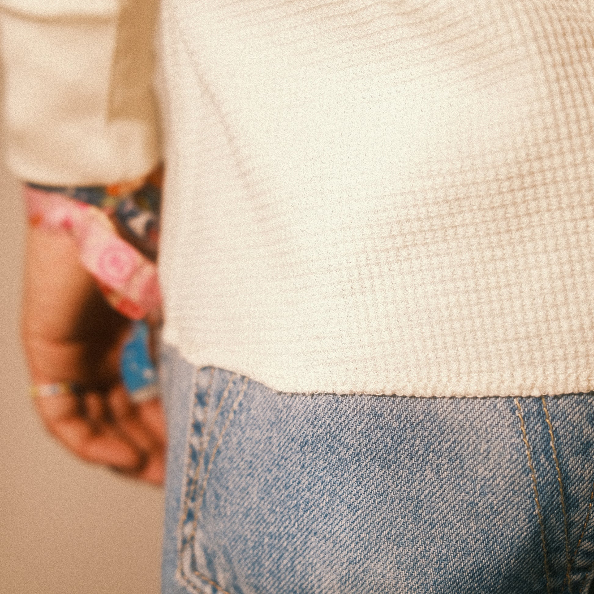Stoffdetail am Saum: fein strukturierter Waffelstrick des cremefarbenen Longsleeves über hellblauer Jeans.
