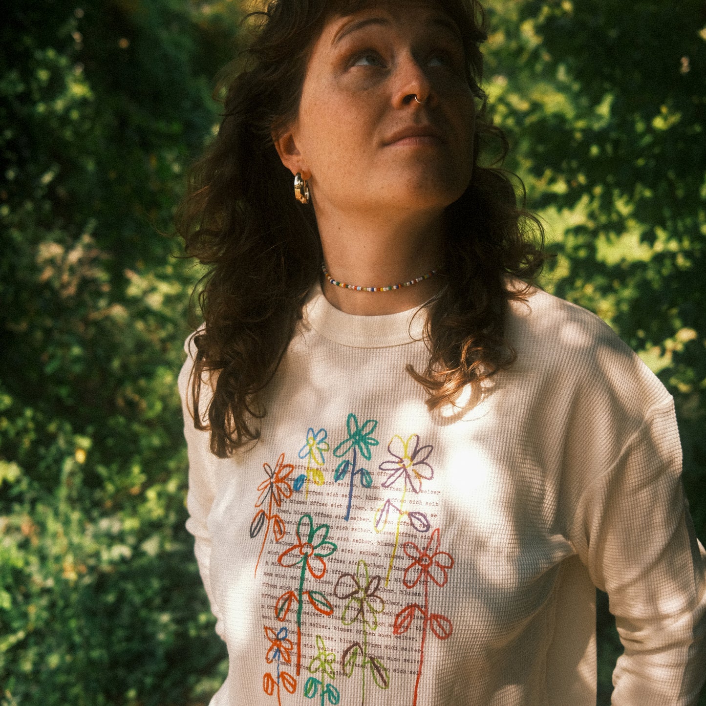 Cremefarbenes Waffelstrick-Longsleeve mit großem, buntem Blumenprint vorn; locker getragen im Freien.