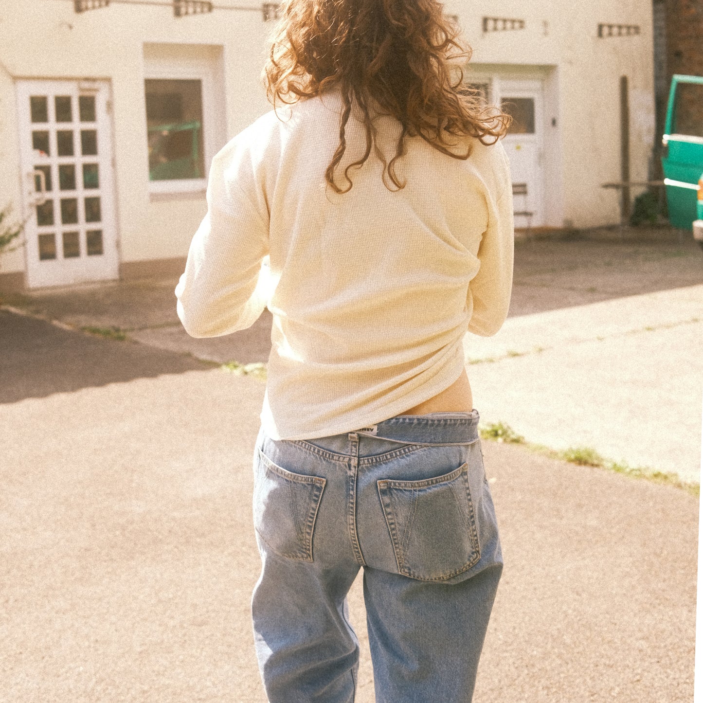 Rückansicht: cremefarbenes Waffelstrick-Longsleeve, lässige Passform über Jeans, Sonnenlicht.