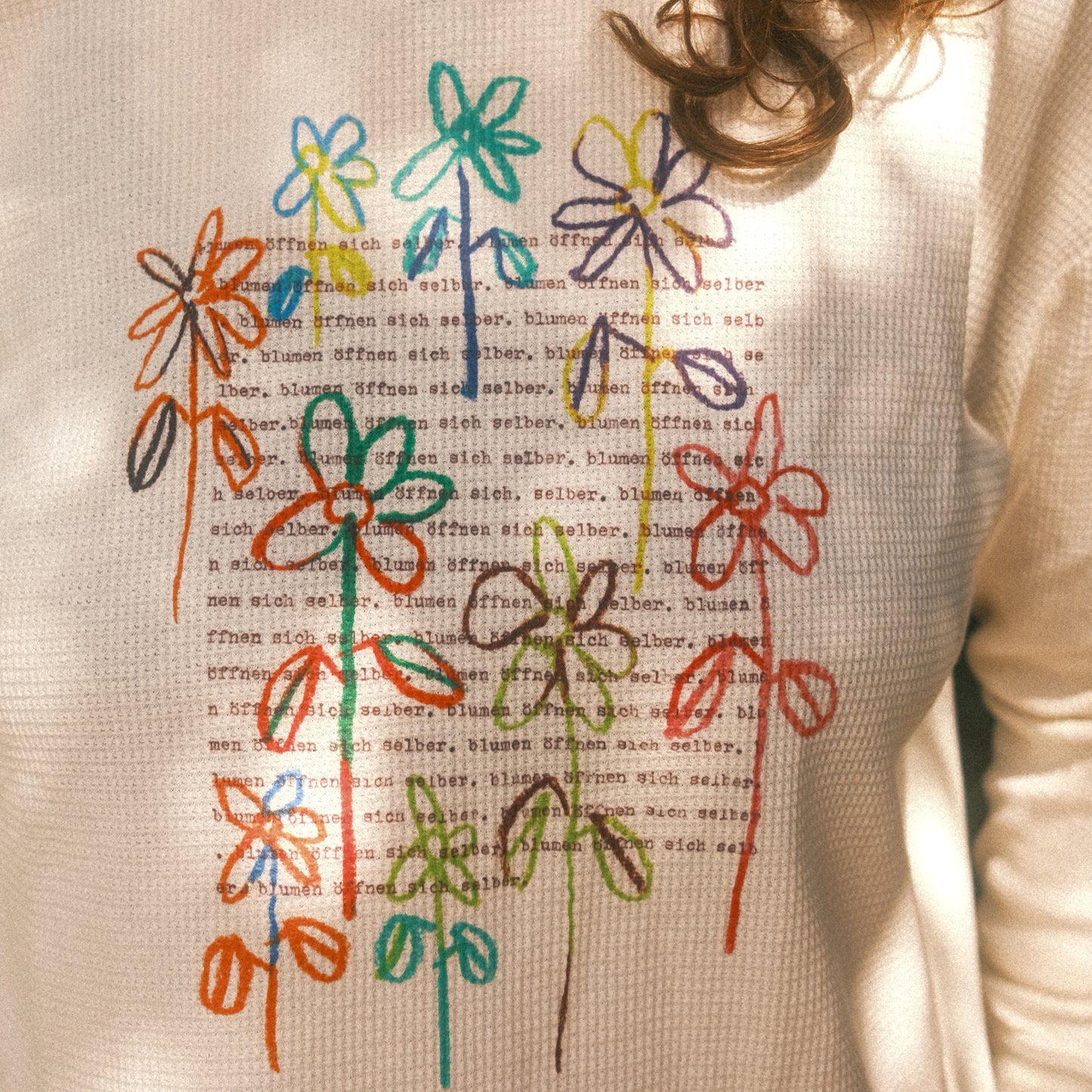 Frontansicht im Studio: cremefarbenes Waffelstrick-Longsleeve mit großem, buntem Blumenmotiv; lockerer Schnitt.