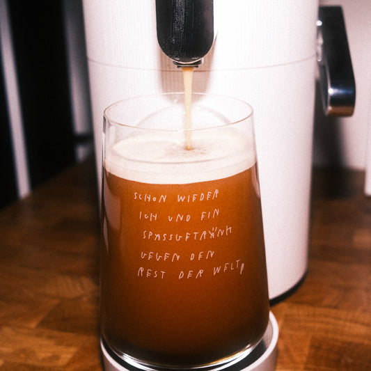 Glas wird unter einem Zapfhahn mit schaumigem, dunkelbraunem Getränk befüllt; auf dem Glas der weiße Schriftzug „schon wieder ich und ein spaßgetränk gegen den rest der welt“.