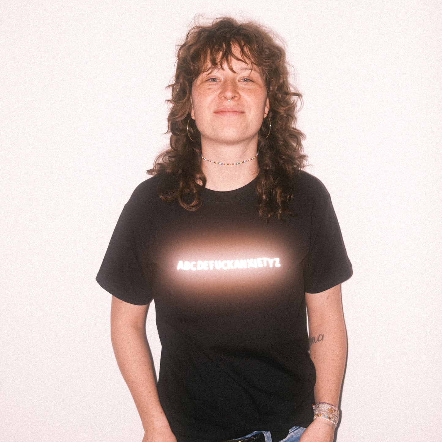 Schwarzes T-Shirt mit reflektierendem Schriftzug in der Brustmitte. Der Schriftzug zeigt die Buchstabenreihe „ABCDEFUCKANXIETYZ“, wobei das Wort „FUCKANXIETY“ besonders hervorgehoben ist.