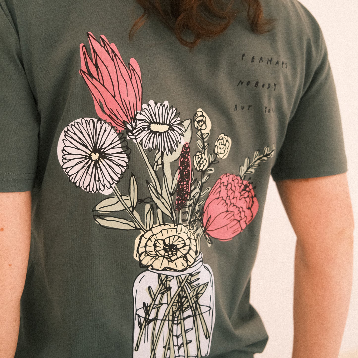 Dunkelgrünes T-Shirt mit kurzen Ärmeln. Auf dem Rücken ist ein großes, buntes Blumenarrangement in einem Glas abgebildet. Rechts daneben steht in schwarzer Handschrift der Text: „perhaps nobody but you“.