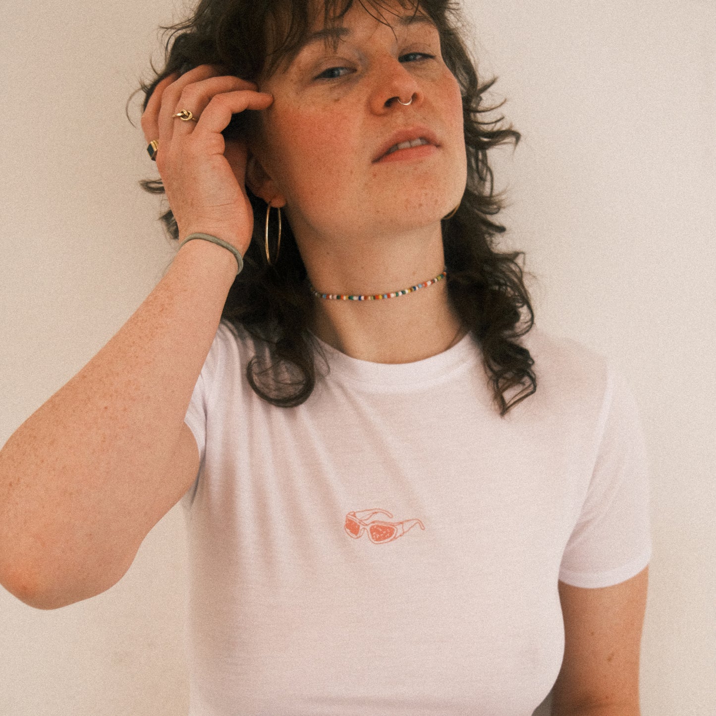 Weißes, kurzes Cropped-T-Shirt mit einem kleinen, rosa Brillen-Print mittig auf der Brust. Das Shirt hat kurze Ärmel und einen klassischen Rundhalsausschnitt.
