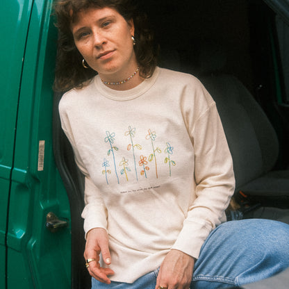 Cremefarbenes Waffelstrick-Longsleeve mit kleinem, buntem Blumenprint auf der Brust; lässig in einer Fahrzeugtür sitzend.