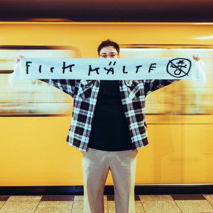 Vorderseite des gleichen weißen Schals mit dem provokanten Schriftzug „FICK KÄLT“ in schwarzer Handschrift sowie einem durchgestrichenen Schneemann-Symbol.