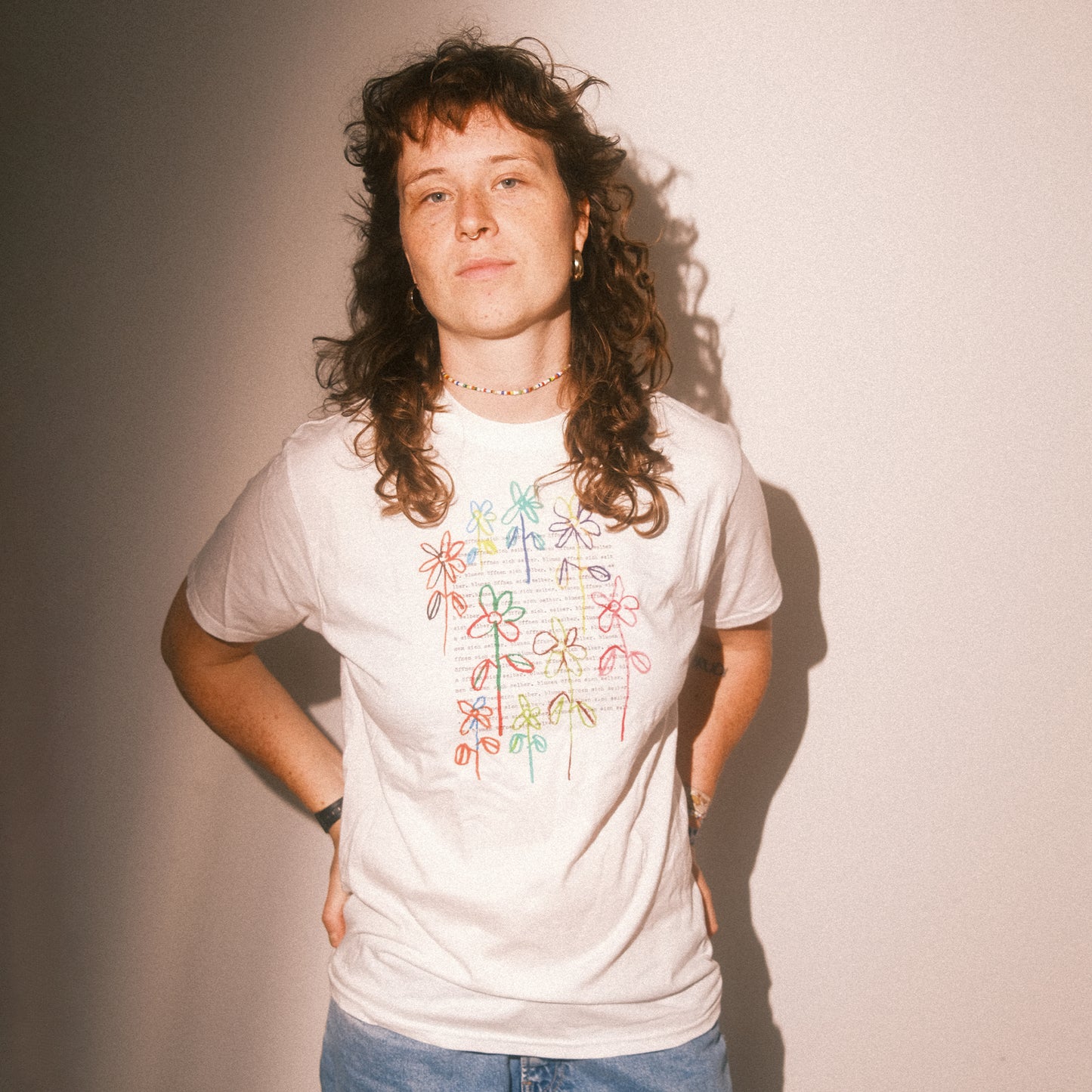 Studio-Frontansicht: weißes T-Shirt mit farbigem Blumenmotiv, gerader Schnitt, kurze Ärmel.