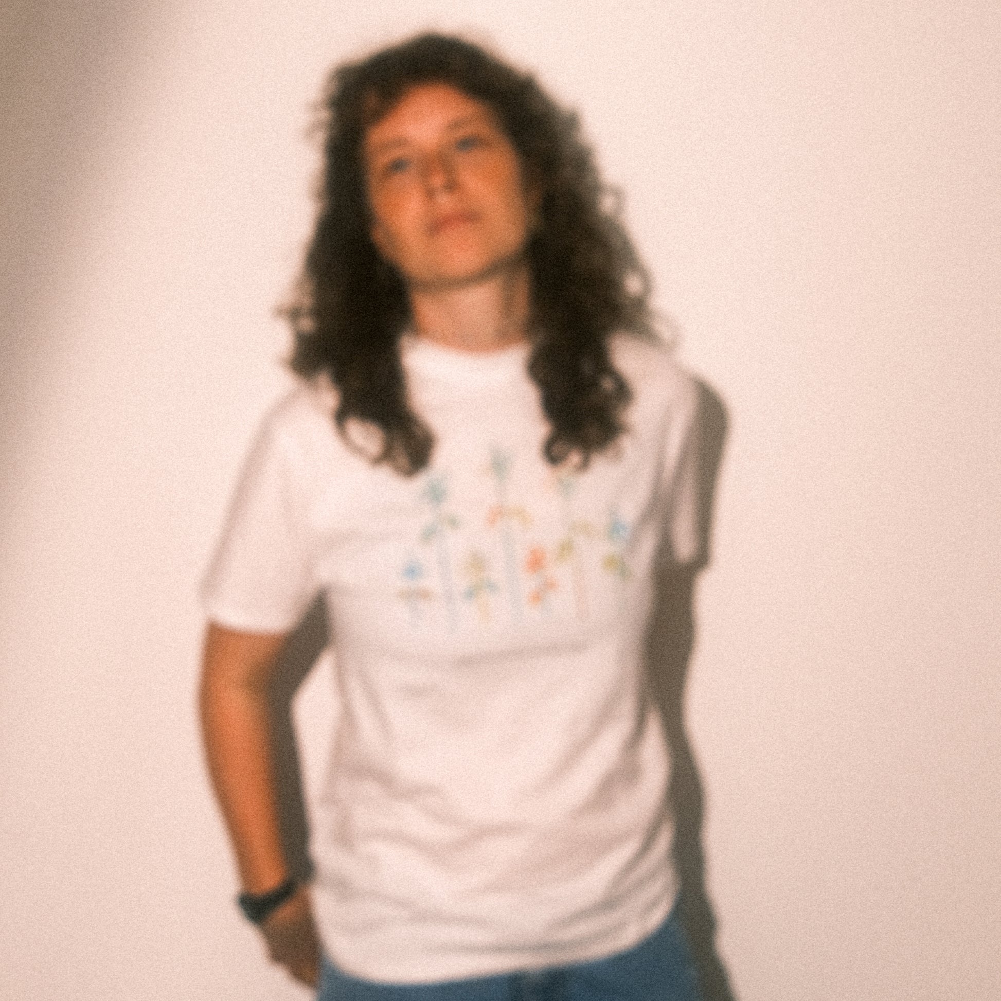 Unscharfes Ganzkörperbild: weißes T-Shirt mit farbigem Blumenprint; Motiv erkennbar, weicher Blur-Effekt.