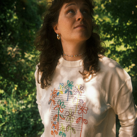 Cremefarbenes Waffelstrick-Longsleeve mit großem, buntem Blumenprint vorn; locker getragen im Freien.