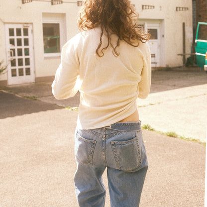 Rückansicht: cremefarbenes Waffelstrick-Longsleeve, lässige Passform über Jeans, Sonnenlicht.
