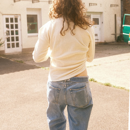 Rückansicht: cremefarbenes Waffelstrick-Longsleeve, lässige Passform über Jeans, Sonnenlicht.