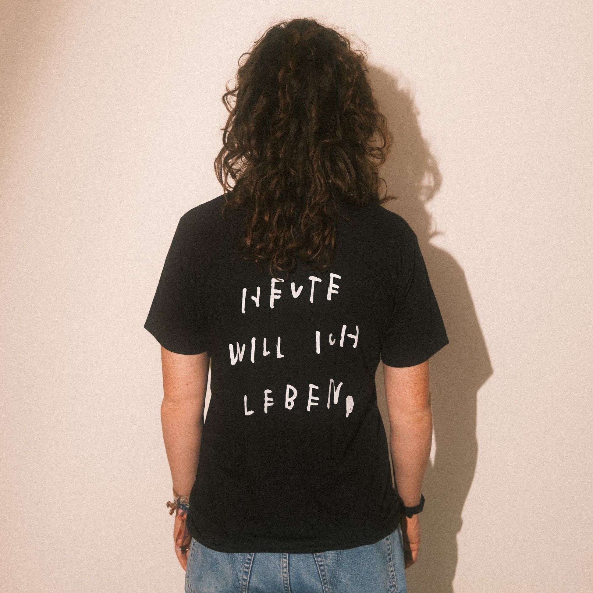 Studio-Rückenansicht: schwarzes T-Shirt, großflächiger weißer Text „HEUTE WILL ICH LEBEN“.