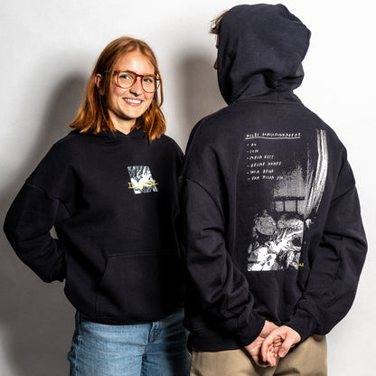 Schwarzer Unisex-Hoodie mit grafischem Print auf Brust und Rückseite. Auf der Vorderseite befindet sich ein kleiner Frontprint mit fragmentarischem Schwarz-Weiß-Motiv, gelber Textzeile und dem Wort „I“ über einem stilisierten Rechteck. Die Rückseite zeigt einen großflächigen Druck mit einem kontrastreichen Schwarz-Weiß-Motiv, das ein Bett mit Textfragmenten kombiniert. Darüber steht in weißer Handschrift: „ALLE DURCHGEKNALLT“ sowie eine Aufzählung: „– DU – ICH – DEIN BETT – DEINE SORGE – WIR ZWEI – VON VORN