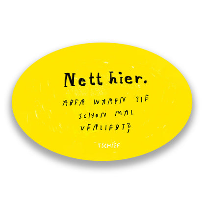 Gelber, ovaler Aufkleber mit schwarzem Schriftzug „Nett hier.“ Darunter handschriftlich ergänzt in Schwarz: „Aber waren Sie schon mal verliebt?“ Unten steht klein „TSCHIEF“. Im Hintergrund unscharf weitere gelbe Aufkleber.