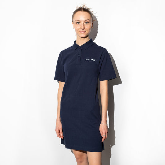 Dunkelblaues Polokleid mit klassischem Kragen und kurzer Knopfleiste, getragen von einer Person vor hellem Hintergrund. Auf der linken Brust ist der Schriftzug „STAY SOFT“ in Weiß aufgestickt. Das Kleid hat eine lockere, gerade Passform und reicht bis über das Knie.

