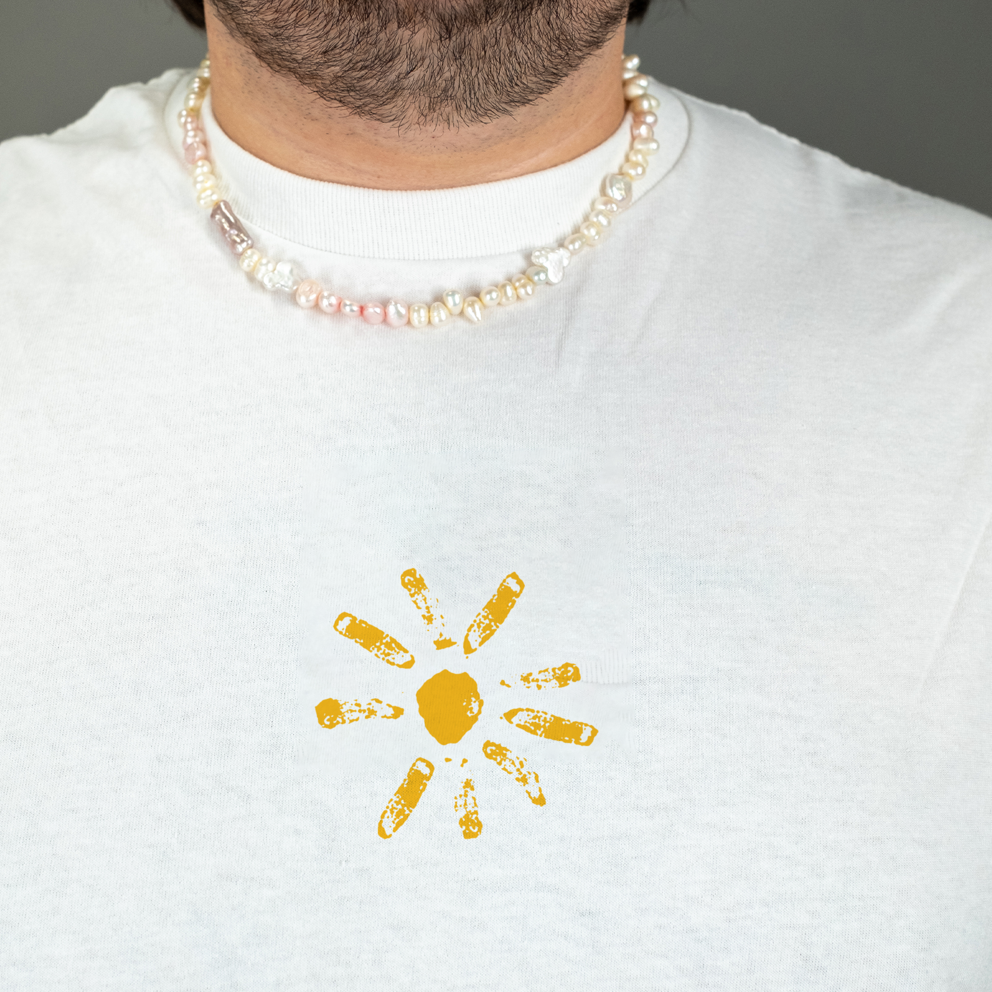 Detailaufnahme der Brustgrafik: Die stilisierte gelbe Sonne ist mittig auf dem weißen T-Shirt platziert. Die Strahlen wirken unregelmäßig und sind wie handgedruckt.