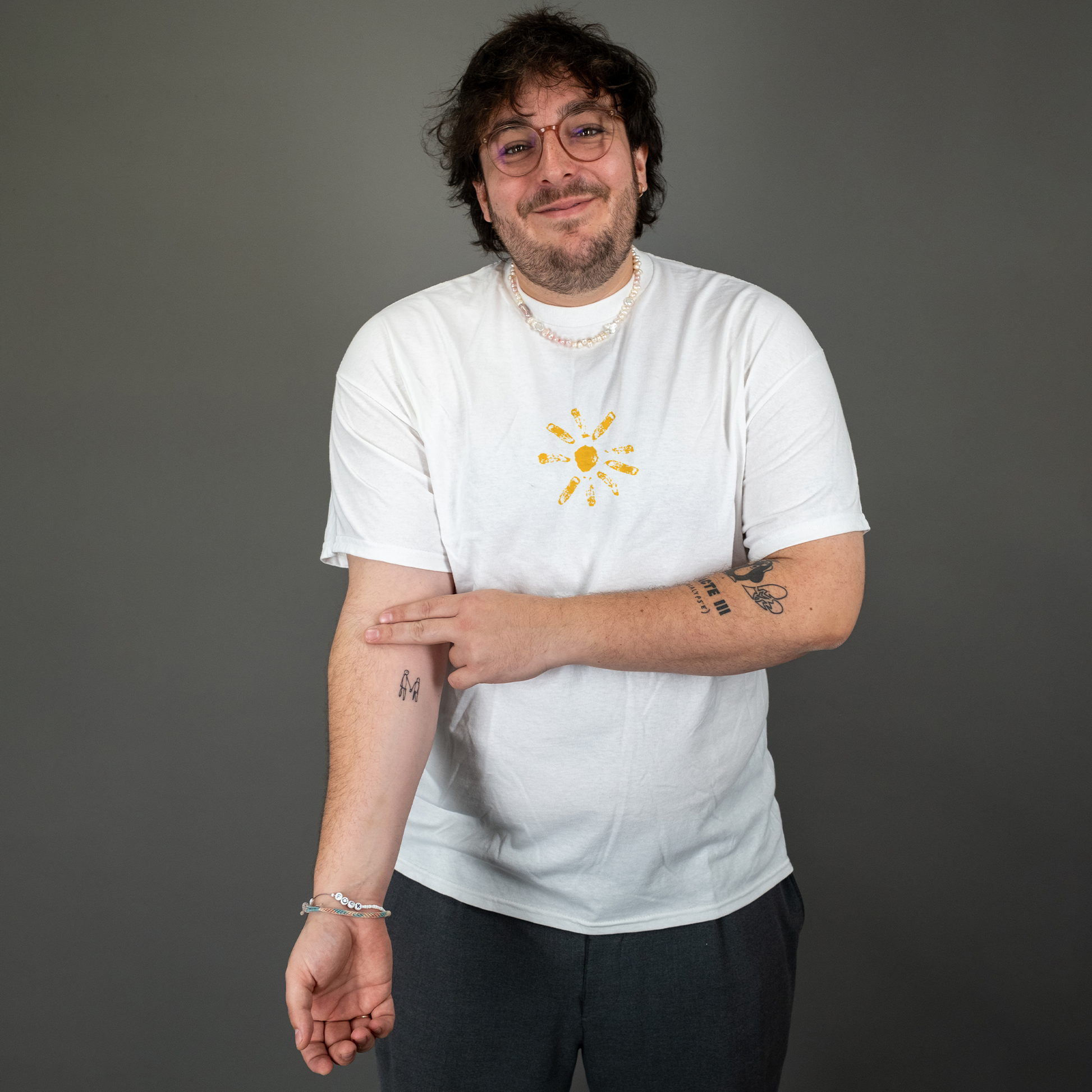 Weißes T-Shirt mit zentralem Frontprint in sonnengelben Tönen, getragen von vorn. Die Brustgrafik zeigt eine stilisierte Sonne mit acht ungleichmäßigen Strahlen um einen mittigen Kreis, gestaltet in handgedruckter Optik.