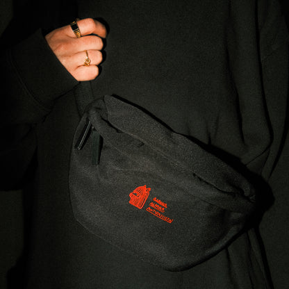 Schwarze Bauchtasche aus robustem Stoff mit Reißverschluss. Auf der Vorderseite ist ein rotes, feingesticktes Logo eines stilisierten Alpaka-Kopfs mit den Schriftzügen „ALPAKA ALPAKA ALPAKA / PERU, THE CLASSIC STA!“ rechts daneben.