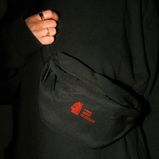Schwarze Bauchtasche aus robustem Stoff mit Reißverschluss. Auf der Vorderseite ist ein rotes, feingesticktes Logo eines stilisierten Alpaka-Kopfs mit den Schriftzügen „ALPAKA ALPAKA ALPAKA / PERU, THE CLASSIC STA!“ rechts daneben.