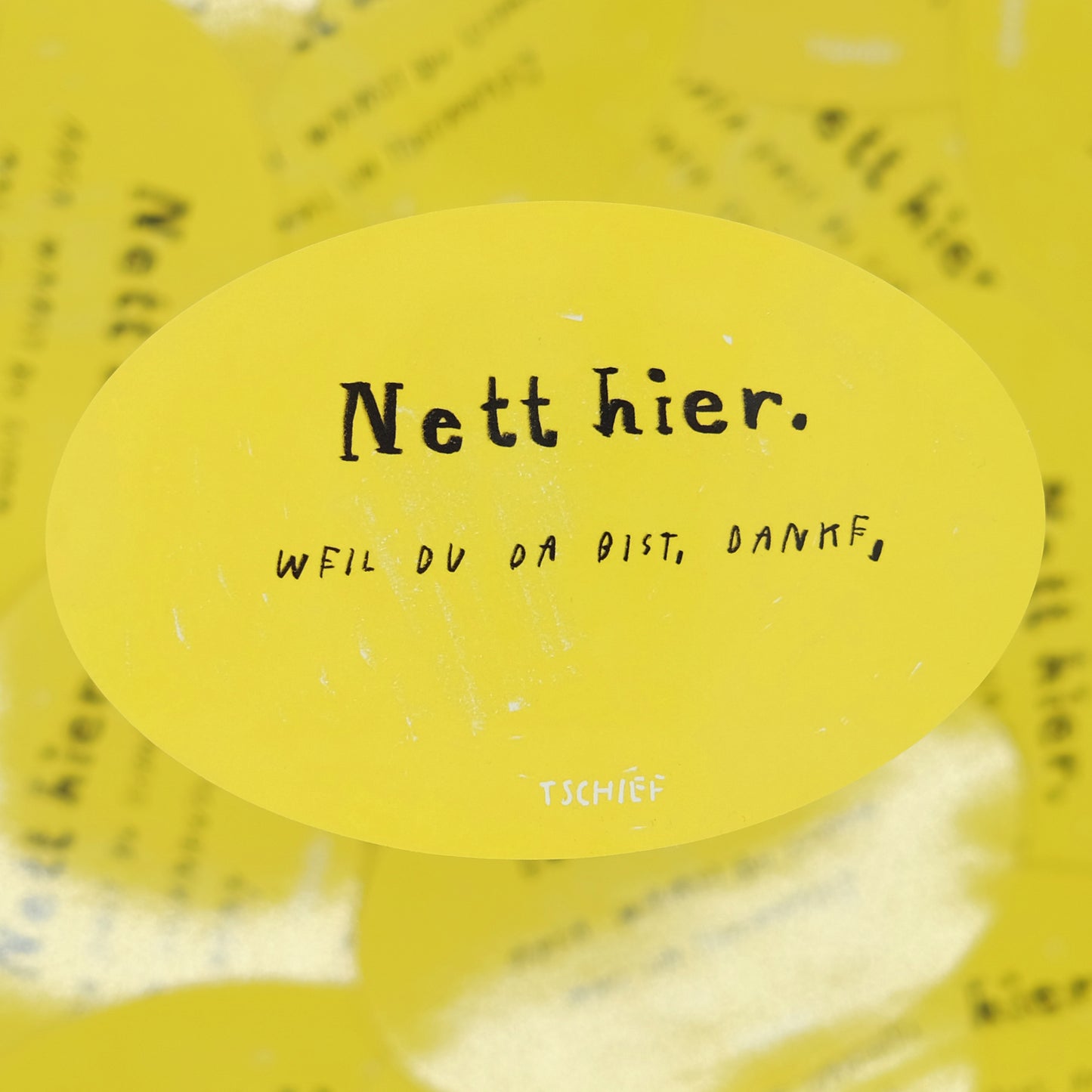 Gelber, ovaler Aufkleber mit schwarzem Schriftzug „Nett hier.“ Darunter handschriftlich ergänzt in Schwarz „Weil du da bist, danke.“ Unten steht klein „TSCHIEF“. Im Hintergrund unscharf weitere gelbe Aufkleber.