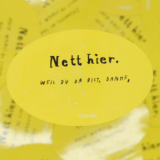 Gelber, ovaler Aufkleber mit schwarzem Schriftzug „Nett hier.“ Darunter handschriftlich ergänzt in Schwarz „Weil du da bist, danke.“ Unten steht klein „TSCHIEF“. Im Hintergrund unscharf weitere gelbe Aufkleber.