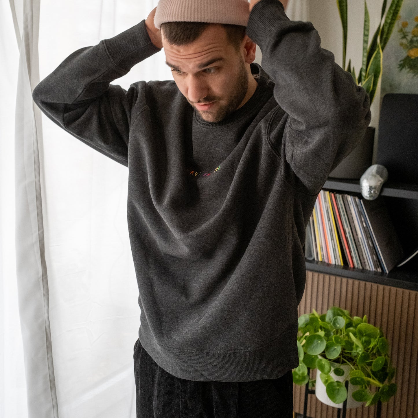 Dunkelgrauer Pullover mit Rundhalsausschnitt. Auf der Brust ist der Schriftzug „FRAGILER ATZF“ in bunten, einzeln bestickten Großbuchstaben zu sehen. Der Pullover hat lange Ärmel und eine normale Passform.