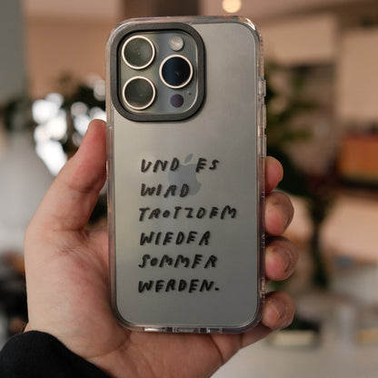 Nahaufnahme einer transparenten Handyhülle mit schwarzer Handschrift. Auf der Hülle steht:
„Und es wird trotzdem wieder Sommer werden.“