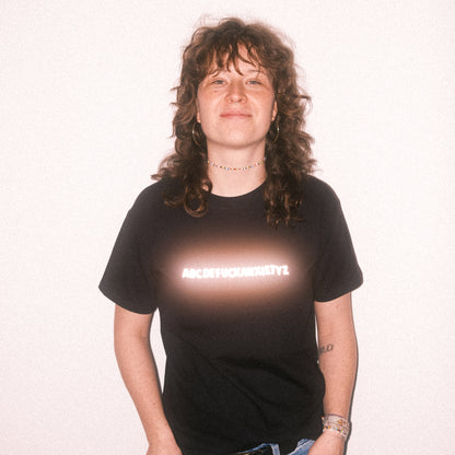 Schwarzes T-Shirt mit reflektierendem Schriftzug in der Brustmitte. Der Schriftzug zeigt die Buchstabenreihe „ABCDEFUCKANXIETYZ“, wobei das Wort „FUCKANXIETY“ besonders hervorgehoben ist.