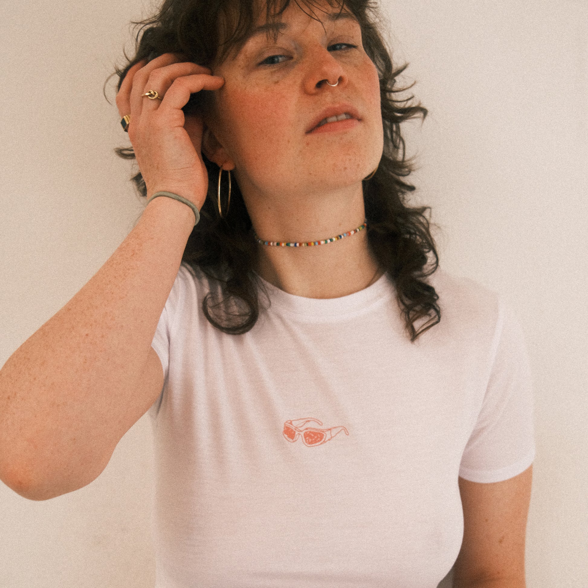 Weißes, kurzes Cropped-T-Shirt mit einem kleinen, rosa Brillen-Print mittig auf der Brust. Das Shirt hat kurze Ärmel und einen klassischen Rundhalsausschnitt.