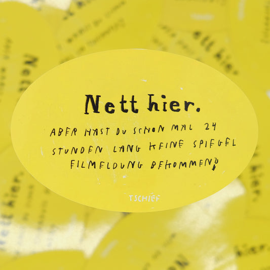 Gelber, ovaler Aufkleber mit schwarzem Schriftzug „Nett hier.“ Darunter handschriftlich ergänzt in Schwarz: „Aber hast du schon mal 24 Stunden lang keine Spielfilmmeldung bekommen?“ Unten steht klein „TSCHIEF“. Im Hintergrund unscharf weitere gelbe Aufkleber.