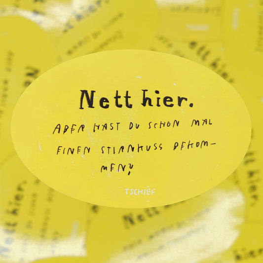 Gelber ovaler Aufkleber mit schwarzer und weißer Schrift. Oben steht in großer Schrift „Nett hier.“ Darunter in handschriftlicher Schrift: „Aber hast du schon mal einen Stirnkuss bekommen?“ Unten mittig steht klein „TSCHIEF“.