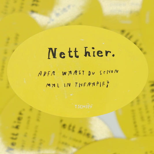 Gelber, ovaler Aufkleber mit schwarzem Schriftzug „Nett hier.“ Darunter handschriftlich ergänzt in Schwarz die Frage: „Aber warst du schon mal in Therapie?“ Unten steht klein „TSCHIEF“. Der Hintergrund zeigt weitere gelbe Aufkleber verschwommen